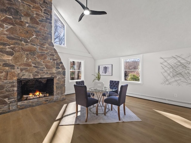 dining space featuring ceiling fan, baseboard heating, a stone fireplace, dark hardwood / wood-style flooring, and high vaulted ceiling