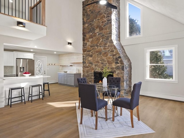 dining area featuring a fireplace, high vaulted ceiling, and light hardwood / wood-style flooring