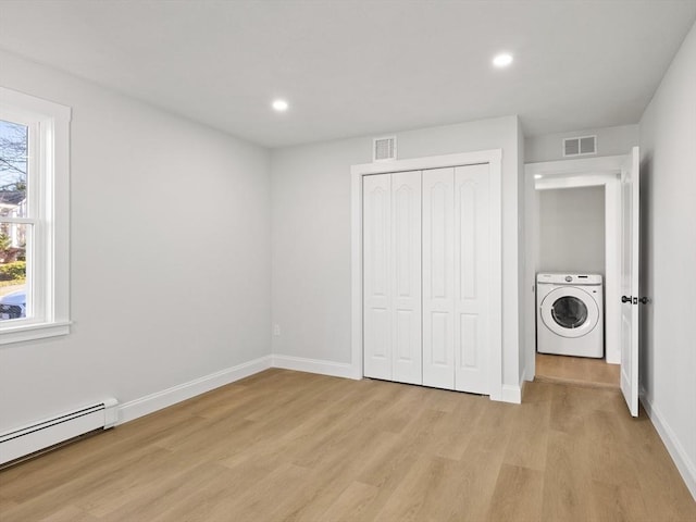 unfurnished bedroom featuring baseboard heating, washer / clothes dryer, a closet, and light hardwood / wood-style floors