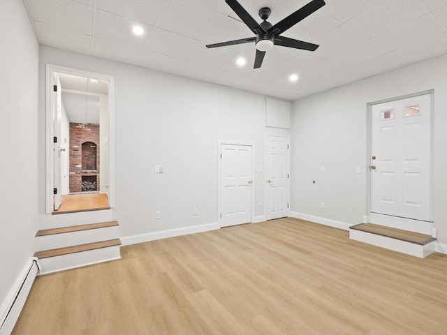 interior space featuring ceiling fan, a fireplace, a baseboard radiator, and light hardwood / wood-style floors