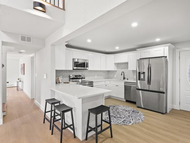 kitchen featuring light wood-type flooring, stainless steel appliances, sink, white cabinets, and a breakfast bar area