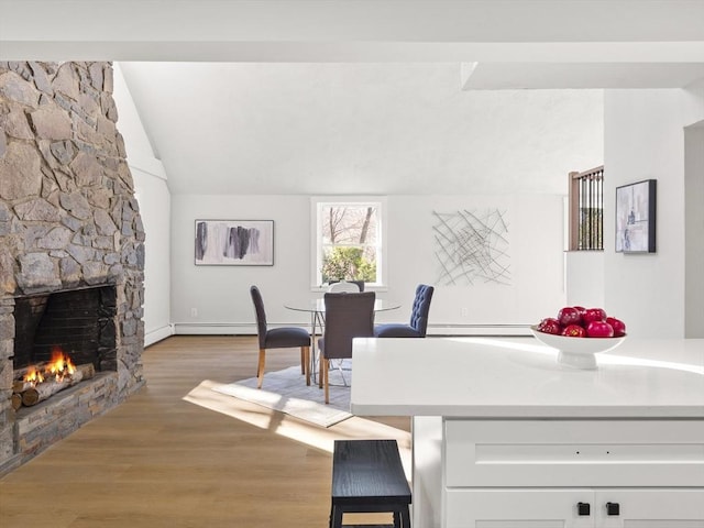 dining space featuring light hardwood / wood-style floors, a stone fireplace, lofted ceiling, and a baseboard heating unit