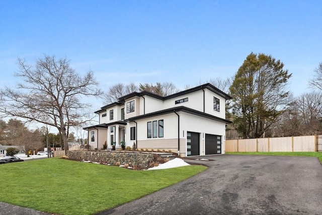 view of front facade with a garage, fence, driveway, stucco siding, and a front yard