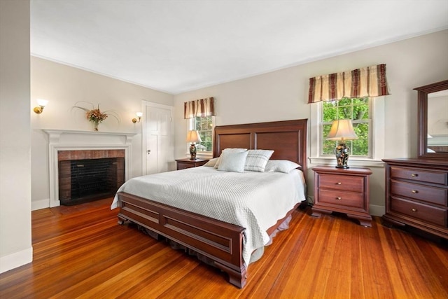 bedroom featuring baseboards, a brick fireplace, and wood finished floors