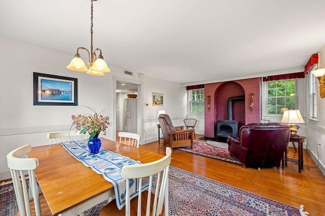 dining space with plenty of natural light, a notable chandelier, wood finished floors, and a wood stove