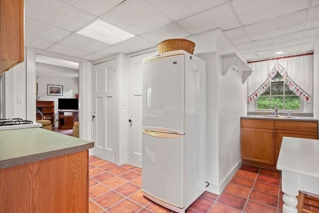 kitchen featuring tile patterned floors, brown cabinetry, freestanding refrigerator, and a sink