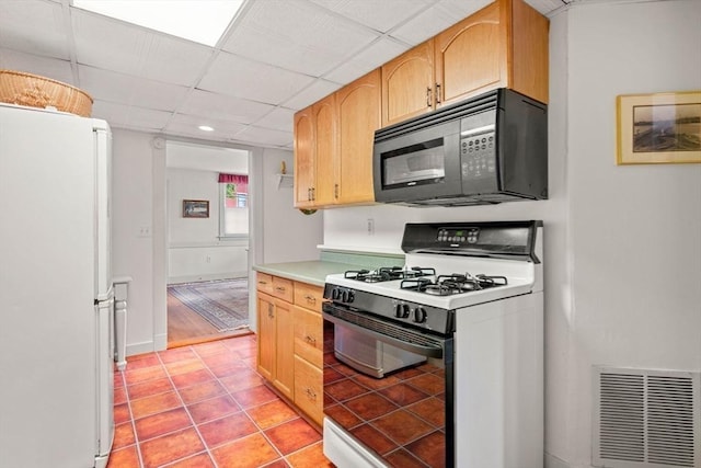 kitchen featuring black microwave, a drop ceiling, gas range oven, light tile patterned floors, and freestanding refrigerator