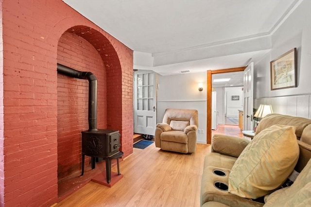 living room with a wood stove, brick wall, and light wood finished floors