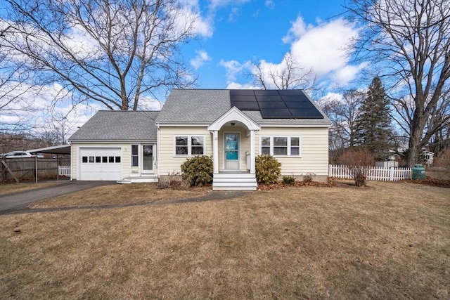 view of front of property featuring driveway, roof mounted solar panels, fence, an attached garage, and a front yard