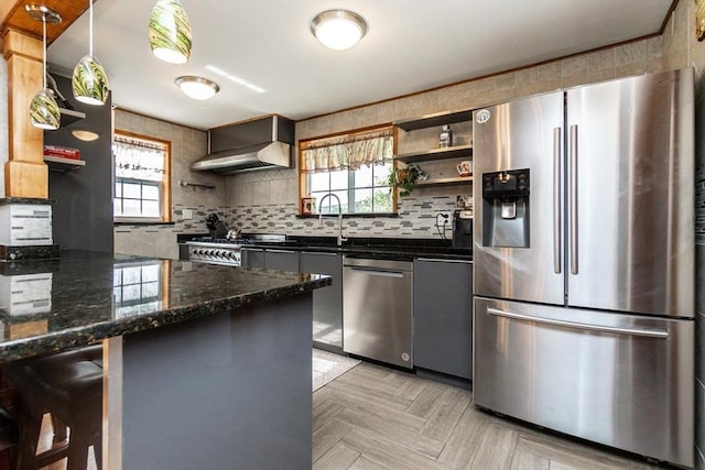 kitchen featuring dark stone counters, wall chimney exhaust hood, tasteful backsplash, open shelves, and appliances with stainless steel finishes