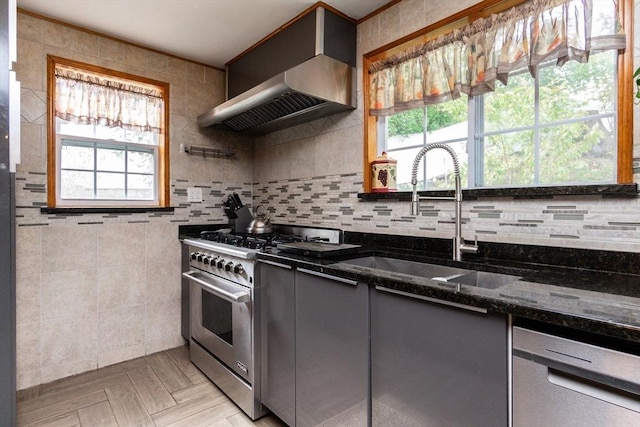 kitchen featuring dark stone counters, wall chimney range hood, a sink, gray cabinetry, and stainless steel range