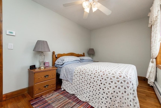 bedroom featuring wood finished floors, a baseboard heating unit, baseboards, and a ceiling fan