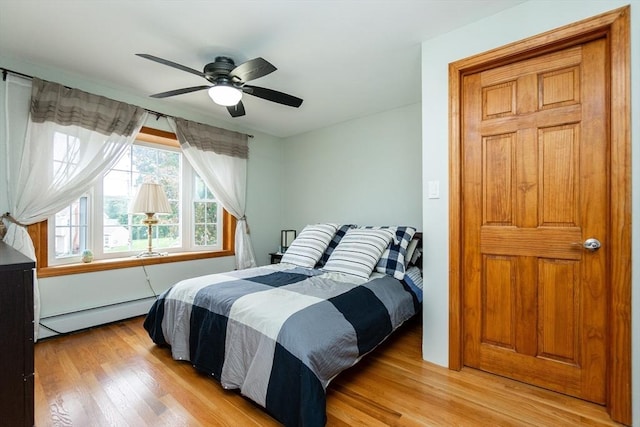 bedroom featuring baseboard heating, light wood-style floors, and a ceiling fan