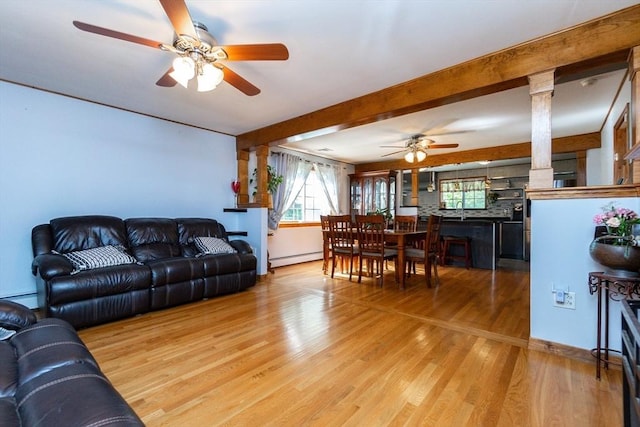 living area featuring baseboard heating, a ceiling fan, beam ceiling, decorative columns, and wood finished floors