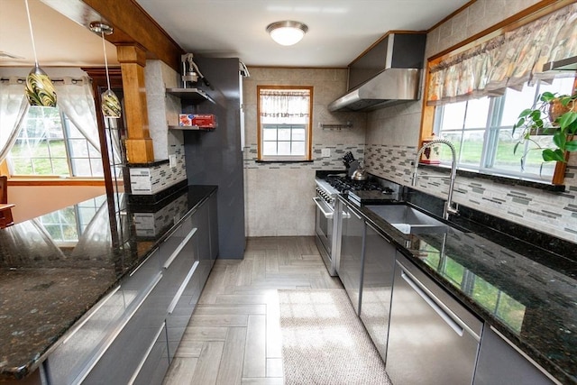 kitchen with wall chimney exhaust hood, tasteful backsplash, open shelves, appliances with stainless steel finishes, and a sink