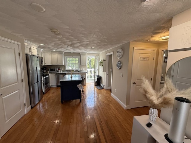146 Main St Unit 2D, Clinton, MA 01510 - kitchen with appliances with stainless steel finishes, white cabinets, dark wood-type flooring, a kitchen island, and baseboards