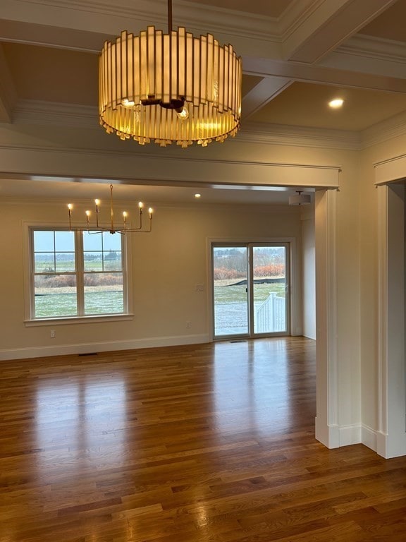 empty room with an inviting chandelier, hardwood / wood-style flooring, crown molding, and a wealth of natural light