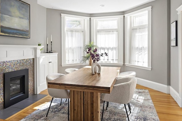 dining area with light wood-type flooring, a tile fireplace, baseboards, and plenty of natural light