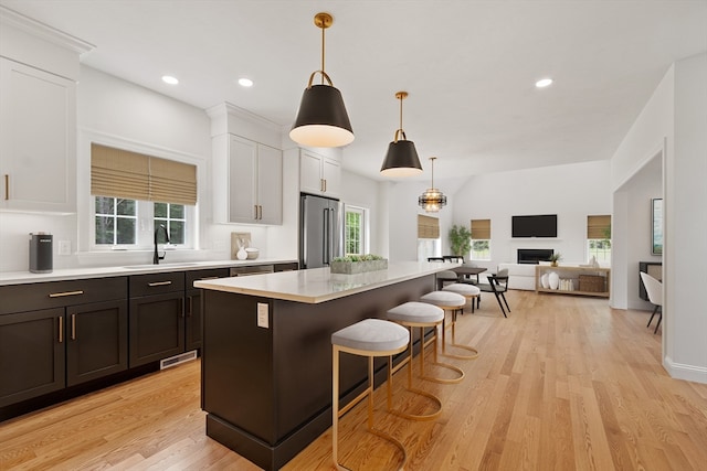 kitchen featuring hanging light fixtures, white cabinetry, stainless steel refrigerator, light wood-type flooring, and a center island