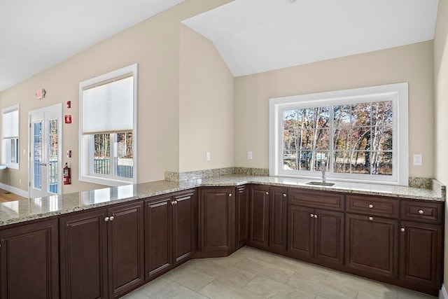 kitchen featuring a wealth of natural light, kitchen peninsula, light stone counters, and sink