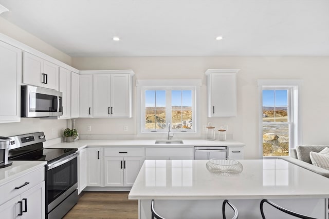 kitchen with appliances with stainless steel finishes, dark hardwood / wood-style floors, a breakfast bar, white cabinetry, and sink