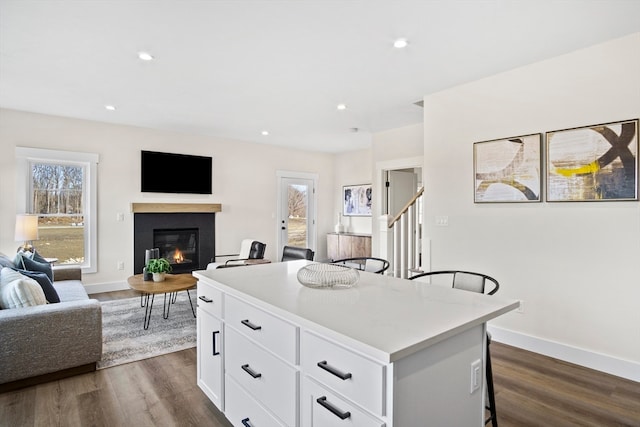 kitchen with dark hardwood / wood-style flooring, a kitchen island, a breakfast bar area, and white cabinets