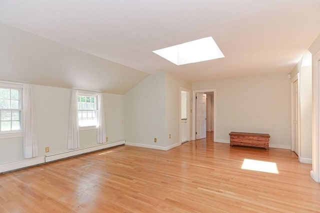 interior space with a baseboard radiator, lofted ceiling with skylight, and light hardwood / wood-style flooring