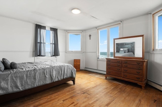 bedroom featuring baseboard heating, a water view, and light hardwood / wood-style flooring