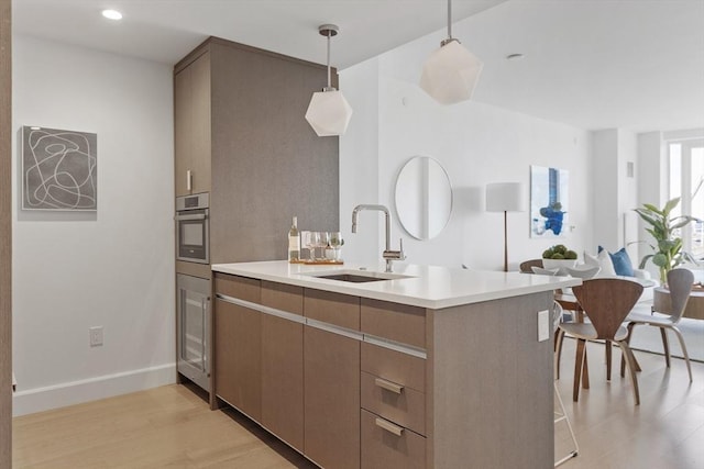 kitchen with oven, sink, decorative light fixtures, light hardwood / wood-style floors, and kitchen peninsula