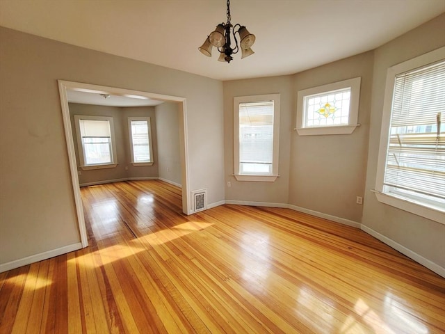 spare room with a chandelier and light wood-type flooring