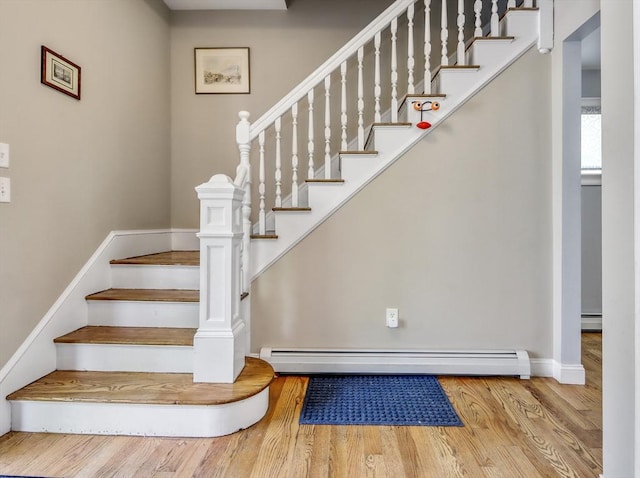stairway featuring a baseboard radiator, wood finished floors, baseboards, and a baseboard heating unit