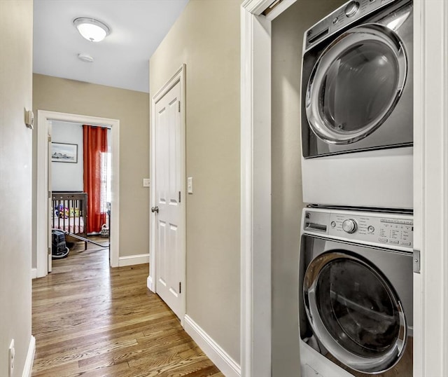 laundry room with stacked washer / drying machine, light wood-style flooring, and baseboards