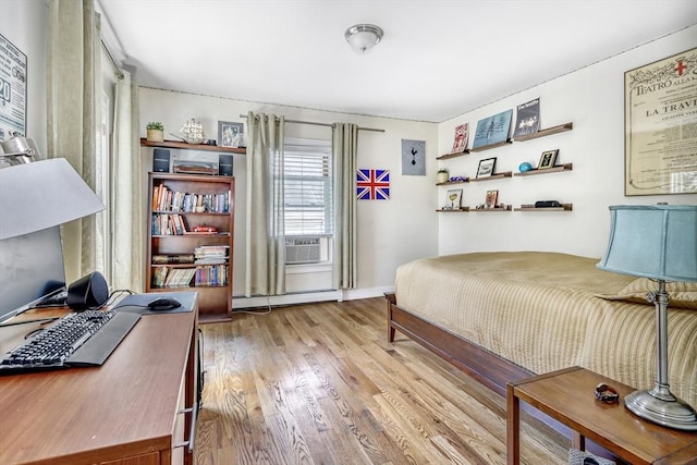 bedroom with a baseboard heating unit, wood finished floors, a desk, and cooling unit