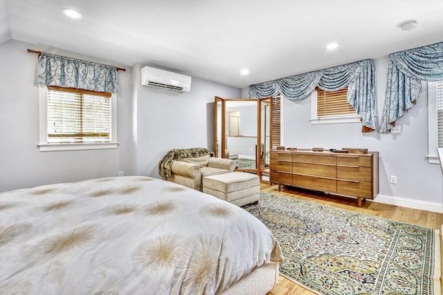bedroom with an AC wall unit, wood finished floors, recessed lighting, and baseboards