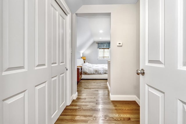 hall with light wood finished floors, baseboards, and vaulted ceiling