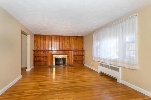 69 Gerald Rd, Milton, MA 02186 - unfurnished living room featuring radiator heating unit, light wood-style flooring, a fireplace, and wooden walls