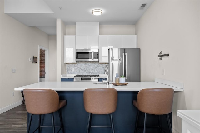 kitchen featuring white cabinets, dark wood-type flooring, backsplash, stainless steel appliances, and a breakfast bar area