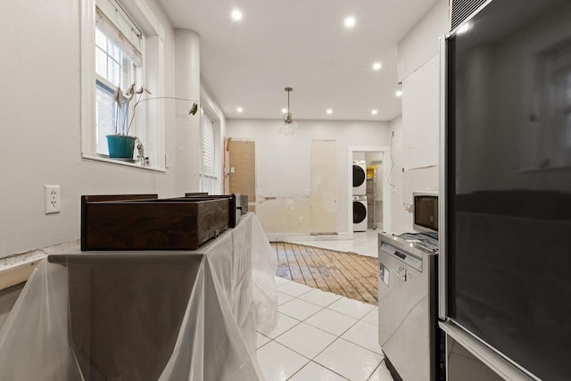 kitchen with decorative light fixtures, white cabinetry, stacked washer / drying machine, light tile patterned floors, and black fridge