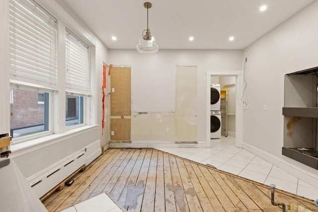 interior space featuring stacked washer and clothes dryer, a baseboard heating unit, and light hardwood / wood-style flooring