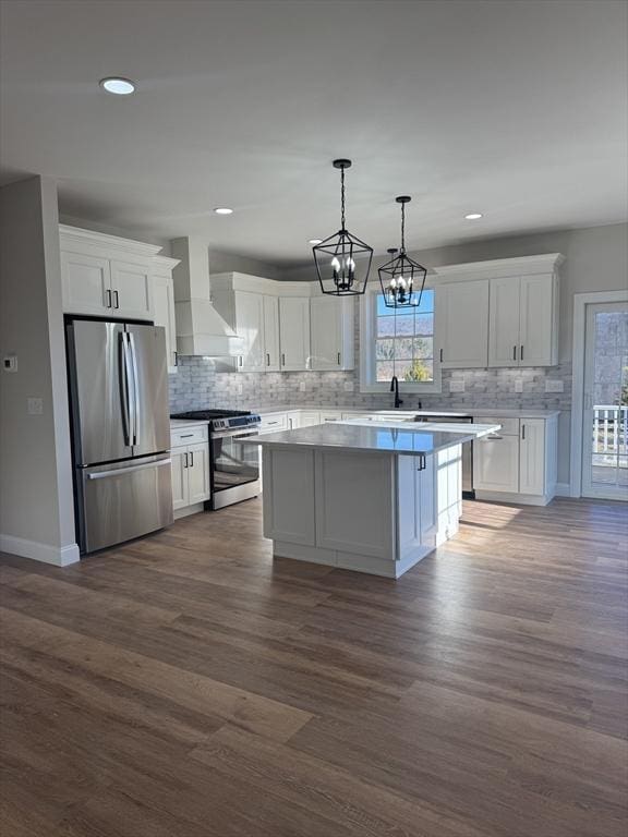 kitchen with stainless steel appliances, white cabinets, custom range hood, a kitchen island, and pendant lighting