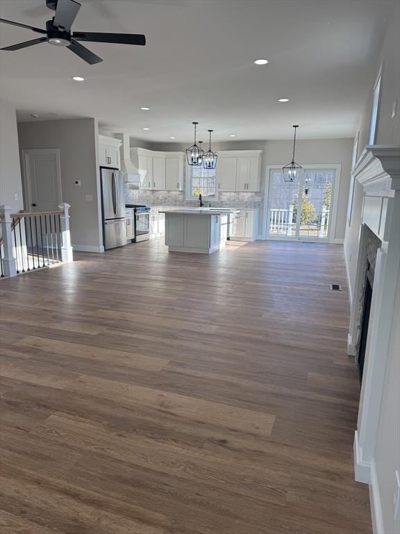 kitchen with decorative light fixtures, white cabinetry, backsplash, a center island with sink, and appliances with stainless steel finishes