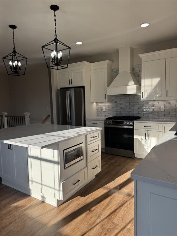 kitchen with stainless steel appliances, hanging light fixtures, custom range hood, hardwood / wood-style flooring, and white cabinets