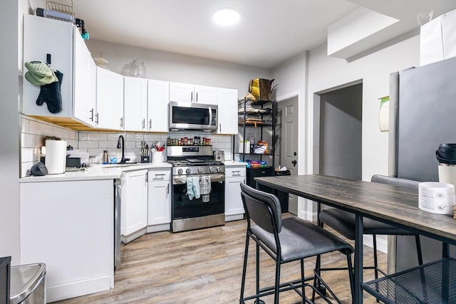 kitchen featuring sink, light hardwood / wood-style flooring, tasteful backsplash, white cabinetry, and stainless steel appliances