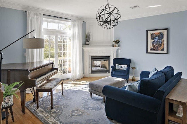living area featuring crown molding, a chandelier, a glass covered fireplace, wood finished floors, and visible vents