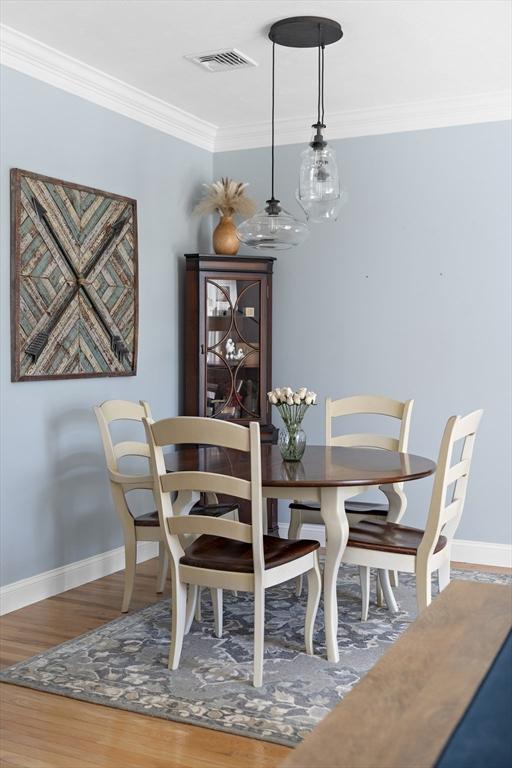 dining space with crown molding, baseboards, visible vents, and wood finished floors