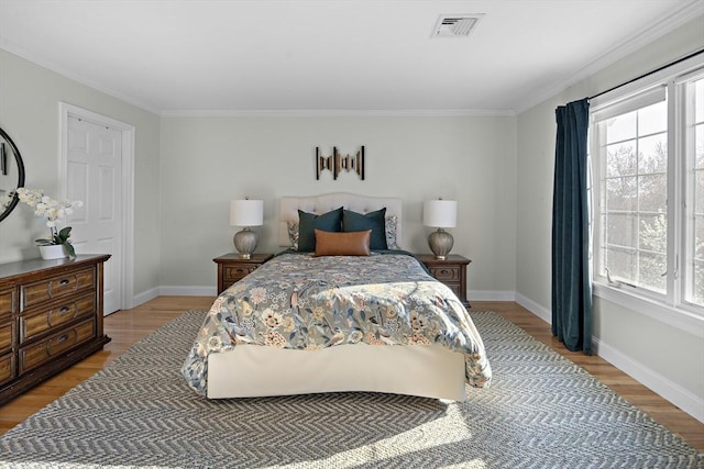 bedroom with light wood-style floors, baseboards, crown molding, and visible vents