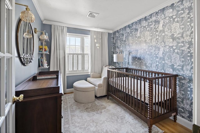 bedroom featuring a crib, baseboards, wood finished floors, visible vents, and ornamental molding