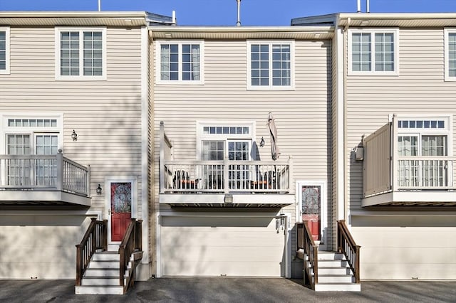 back of house with an attached garage, a balcony, and aphalt driveway