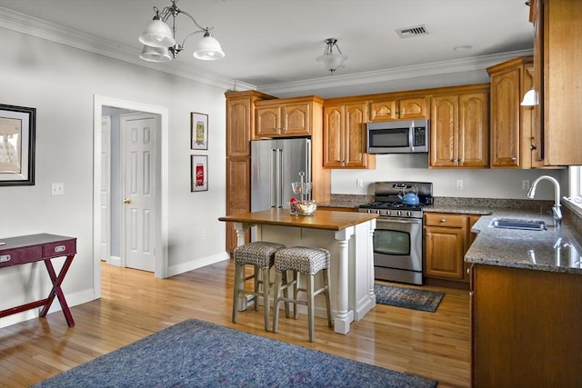 kitchen with a breakfast bar area, appliances with stainless steel finishes, brown cabinets, light wood-type flooring, and a sink