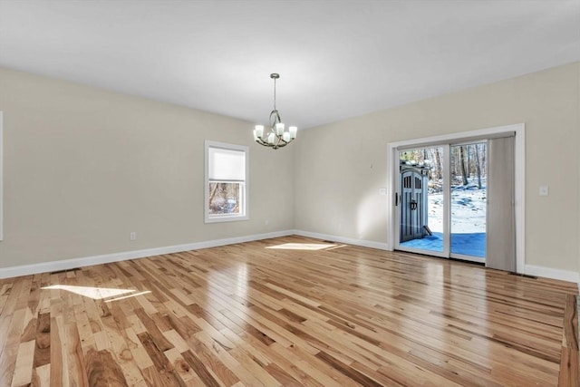 spare room with light wood-style floors, a notable chandelier, and baseboards